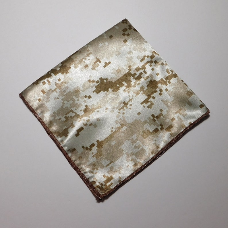 May include: A white and brown camouflage patterned pocket square with a brown border.