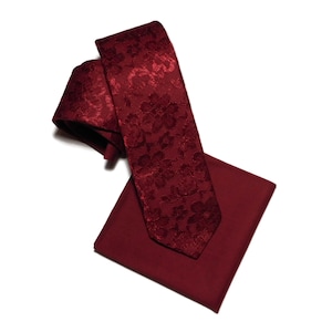 May include: A burgundy tie and pocket square set. The tie has a floral pattern, and the pocket square is a solid colour. The set is displayed on a white background.