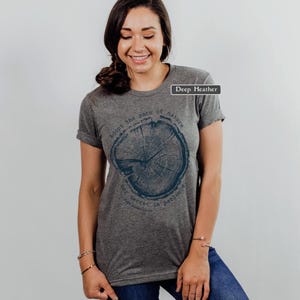 May include: Deep heather gray t-shirt with a dark blue tree ring graphic. The text around the graphic reads "adopt the pace of nature, her secret is patience". The shirt has rolled-up sleeves.