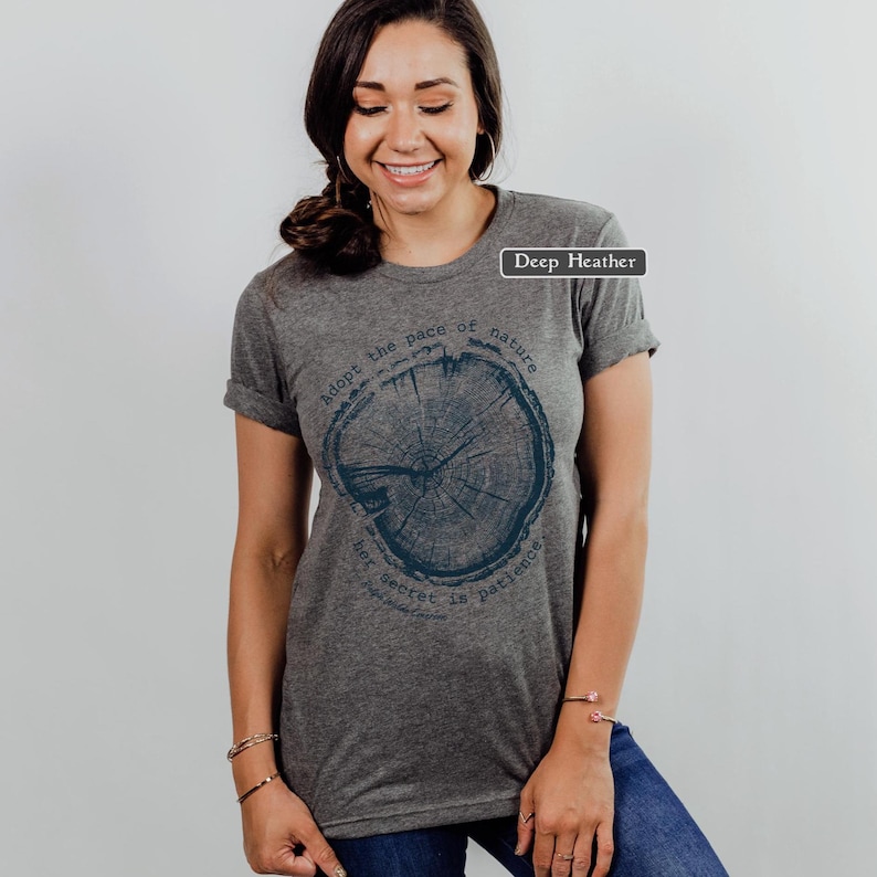 May include: Deep heather gray t-shirt with a dark blue tree ring graphic. The text around the graphic reads "adopt the pace of nature, her secret is patience". The shirt has rolled-up sleeves.