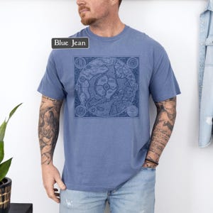 May include: A blue jean t-shirt with a vintage map print on the front. The map is in black and white and shows the world. The shirt is a relaxed fit and has a crew neck.