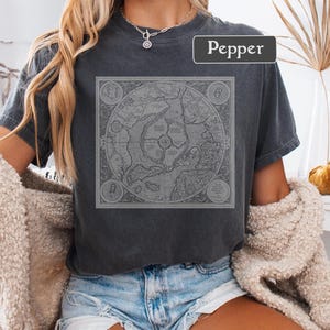 May include: A dark gray t-shirt with a vintage map design printed on the front. The map is in black and white and features a circular design with landmasses and water bodies. The word "Pepper" is printed in white on the top right corner of the shirt.