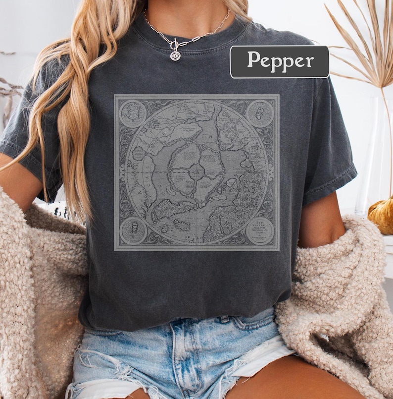 May include: A dark gray t-shirt with a vintage map design printed on the front. The map is in black and white and features a circular design with landmasses and water bodies. The word "Pepper" is printed in white on the top right corner of the shirt.