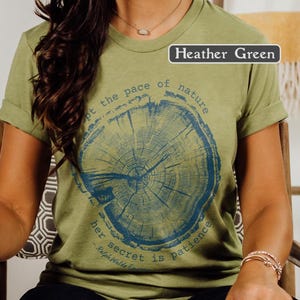 May include: Heather green t-shirt with a blue tree ring graphic. The graphic includes the text "Adopt the pace of nature, her secret is patience - Ralph Waldo Emerson."