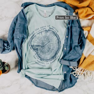 May include: A light blue t-shirt with a tree ring graphic and the text "Adopt the pace of nature, her secret is patience." The shirt is paired with a blue denim shirt. The color of the t-shirt is Prism Ice Blue.
