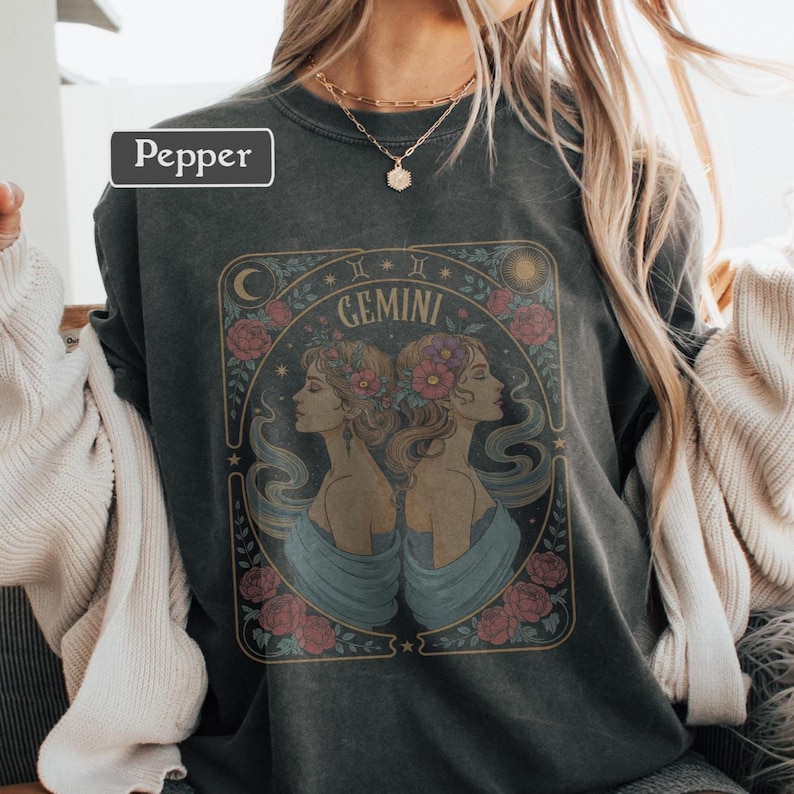 Puede incluir: Sudadera gris oscuro con un dise&ntilde;o del signo zodiacal G&eacute;minis. El gr&aacute;fico incluye dos perfiles de mujeres, flores y elementos celestiales. La palabra "Gemini" se muestra encima de los perfiles. La palabra "Pepper" est&aacute; en un cuadro blanco.
