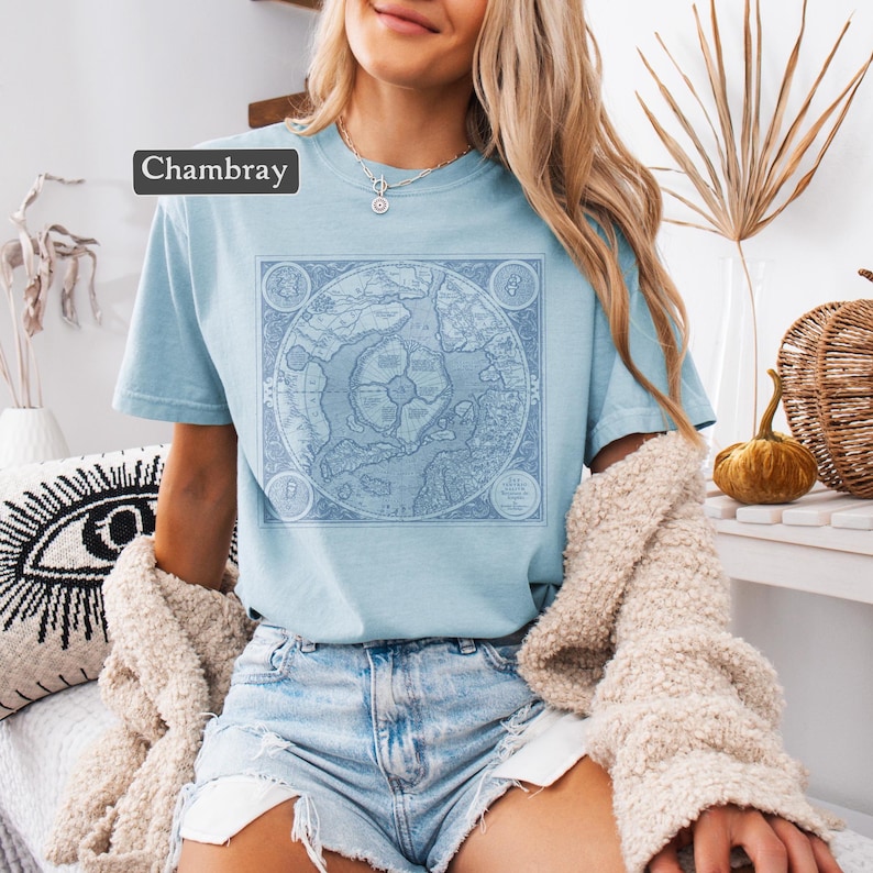 May include: A light blue t-shirt with a vintage map design printed on the front. The map is in shades of blue and white and features a compass rose and other details. The shirt is made of a soft, comfortable fabric and has a relaxed fit.