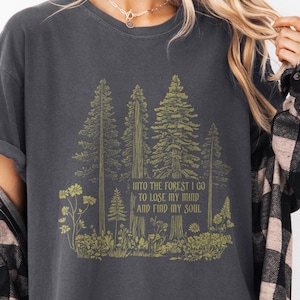May include: A dark gray t-shirt with a graphic of trees and flowers. The text on the shirt reads "Into the forest I go to lose my mind and find my soul."