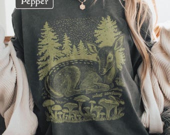 Op de afbeelding: Donkergrijze sweatshirt met een grafische afbeelding van een bosscène. Het ontwerp toont een hert, bomen, paddenstoelen en de woorden "silent sanctuary". Het woord "Pepper" staat in een witte rechthoek linksboven.