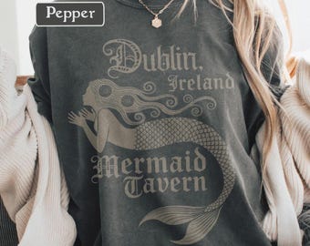 May include: Pepper-colored sweatshirt featuring a mermaid design with the text "Dublin, Ireland Mermaid Tavern" in a vintage style. The sweatshirt has a crew neck and long sleeves. The word "Pepper" is in a white rectangle in the upper left corner.
