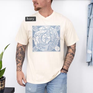 May include: A cream colored t-shirt with a vintage map print in blue. The map is centered on the shirt and is surrounded by a square border. The text "Ivory" is visible in the top left corner of the image.