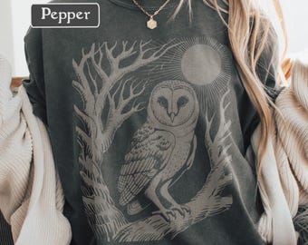 May include: A dark gray sweatshirt with a graphic of an owl perched on a branch, framed by tree branches and a sun. The word "Pepper" is in a white box in the upper left corner. The design is in a lighter gray color.