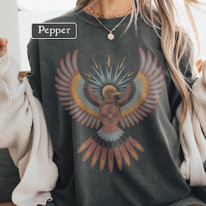 Può includere: Una t-shirt girocollo grigio antracite con la grafica di un uccello stilizzato con le ali spiegate nei toni del rosso, giallo e blu. L'uccello presenta un emblema circolare sul petto. La parola Pepper è stampata in un riquadro bianco in alto a sinistra.