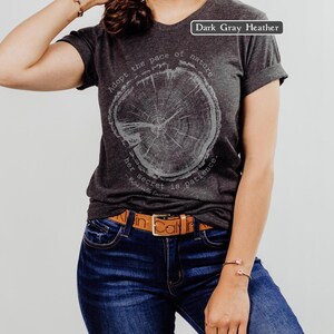 May include: Dark gray heather V-neck t-shirt with a tree ring graphic. The text on the shirt reads "Adopt the pace of nature, her secret is patience." The model is wearing a brown belt and blue jeans.
