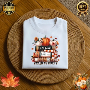 May include: White crew neck sweatshirt with a fall-themed graphic. The design features a stack of books, pumpkins, and fall foliage. Text includes "Just a Girl who loves Fall" and "Hello Pumpkin".
