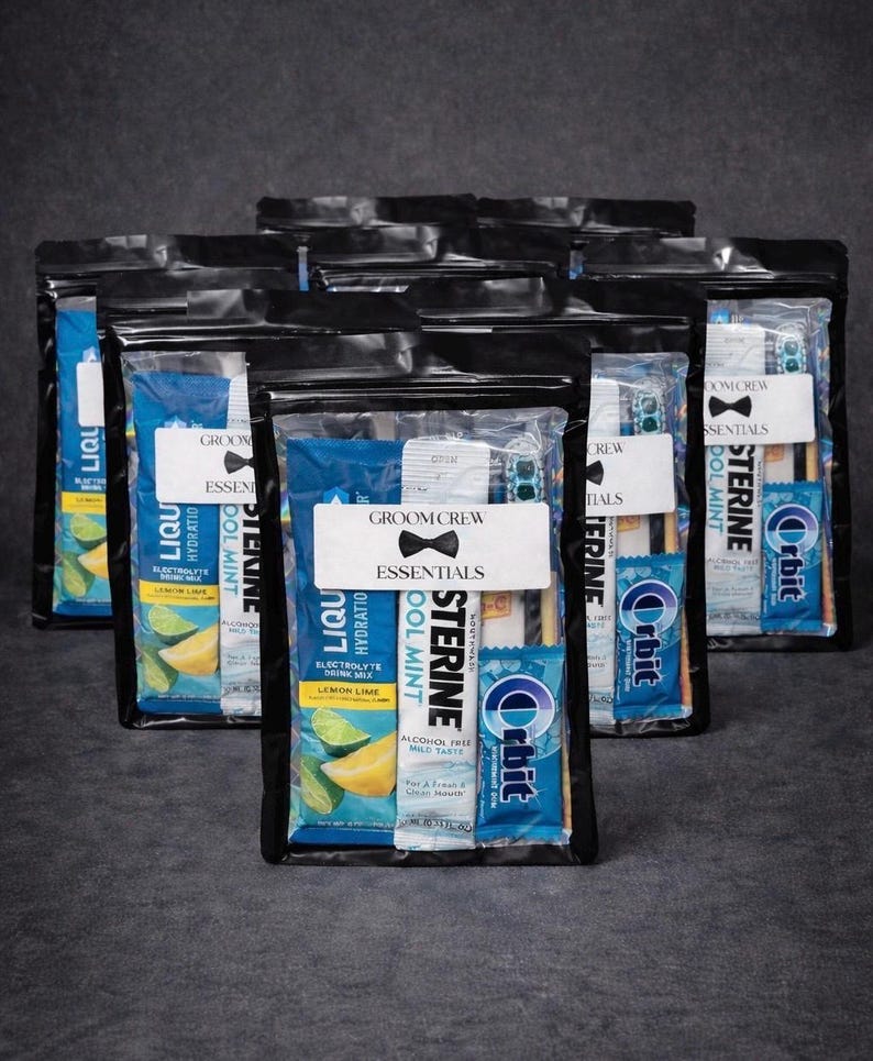 May include: Several black zippered pouches filled with grooming essentials. Each pouch contains items like mouthwash, gum, and electrolyte drink mix. The pouches have a white label that reads "GROOM CREW ESSENTIALS" with a bow tie graphic.