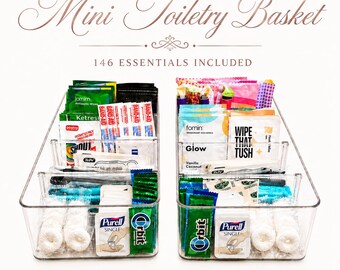 May include: Two clear plastic rectangular bins filled with assorted personal care items. The text "Mini Toiletry Basket" and "146 ESSENTIALS INCLUDED" appears above the bins. The contents include various small packets, wipes, and hygiene products.