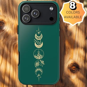 May include: A dark green phone case with a gold celestial design featuring moon phases and stars. The case has a camera cutout and a button that says "8 Colors Available". The case is on a wooden surface.