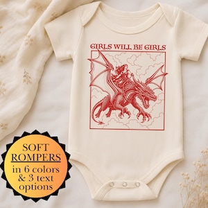 Puede incluir: Un body de manga corta color crema con un estampado gr&aacute;fico rojo de una persona montando un drag&oacute;n entre nubes. El texto GIRLS WILL BE GIRLS aparece sobre la ilustraci&oacute;n. Una insignia negra en forma de estrella muestra texto informativo.