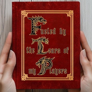 Könnte beinhalten: Ein rotes Notizbuch mit goldenem Rand und dem Text "Fueled by the Tears of my Players" in einer dekorativen Schriftart. Das Cover zeigt Drachenillustrationen in den Buchstaben. Das Notizbuch wird von zwei Händen gehalten.