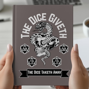 May include: A grey journal featuring the text "THE DICE GIVETH" and "THE DICE TAKETH AWAY". The cover displays a skull entwined with a snake, and dice symbols. The journal is held by a person.