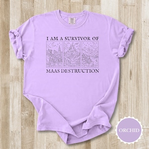K&ouml;nnte beinhalten: Orchideenfarbenes T-Shirt mit dem Text "I AM A SURVIVOR OF MAAS DESTRUCTION". Das Design zeigt drei illustrierte Tafeln: Crescent City, Terrasen und Velaris. Das Shirt besteht aus einem weichen, bequemen Material.