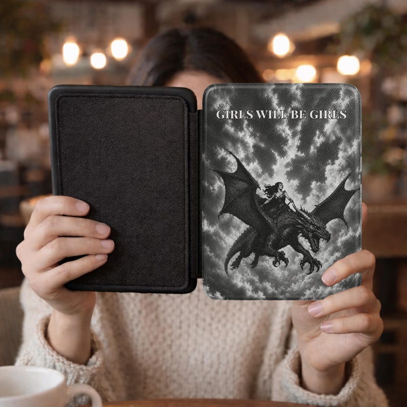 May include: A black e-reader case featuring a monochrome graphic of a figure riding a dragon against a cloudy sky. The text "GIRLS WILL BE GIRLS" is printed in white capital letters at the top. The case has a solid black interior lining.