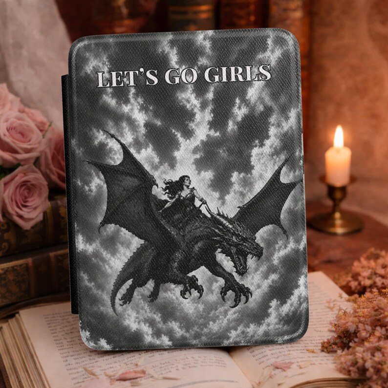 May include: A rectangular e-reader case featuring a black and white graphic of a person riding a dragon against a cloudy sky. The text LET'S GO GIRLS is printed in white at the top. The case has a textured surface and rounded corners.