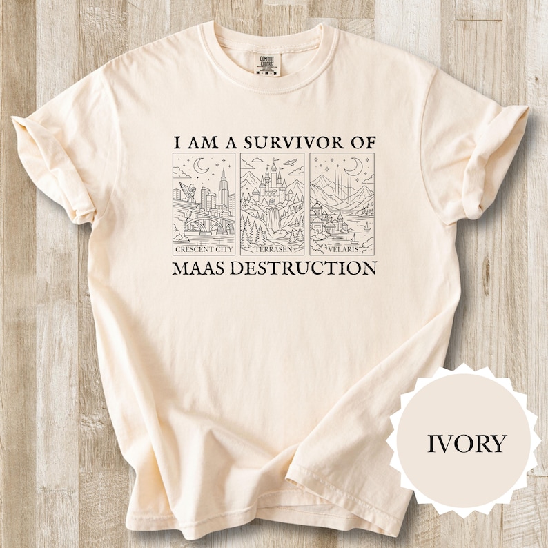 K&ouml;nnte beinhalten: Elfenbeinfarbenes T-Shirt mit dem Text "I AM A SURVIVOR OF MAAS DESTRUCTION" und drei illustrierten Tafeln. Die Tafeln zeigen Stadt- und Landschaftsbilder. Das T-Shirt ist gefaltet, mit sichtbarem &Auml;rmel und einem "IVORY" Farbetikett.