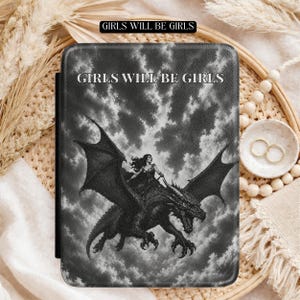 May include: A rectangular e-reader case featuring a black and white graphic of a person riding a dragon against a cloudy sky. The text "GIRLS WILL BE GIRLS" is printed in white capital letters at the top centre of the textured cover surface.