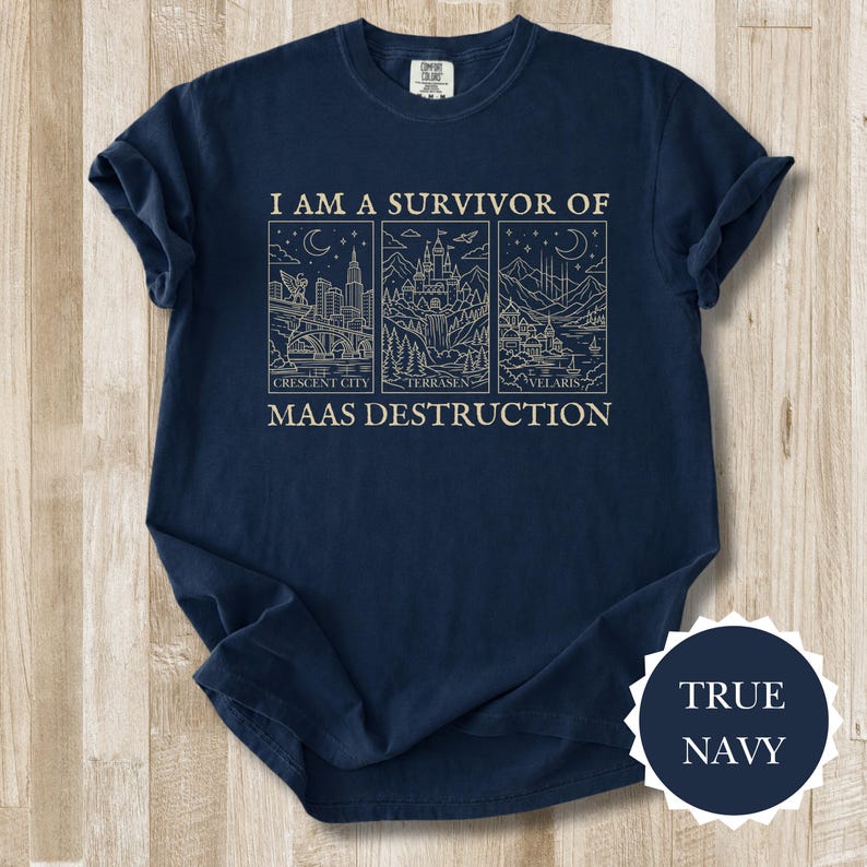 K&ouml;nnte beinhalten: Marineblaues T-Shirt mit dem Text "I AM A SURVIVOR OF MAAS DESTRUCTION" und drei illustrierten Tafeln. Die Tafeln zeigen Stadtlandschaften und Landschaften. Das T-Shirt hat einen Rundhalsausschnitt und kurze &Auml;rmel.