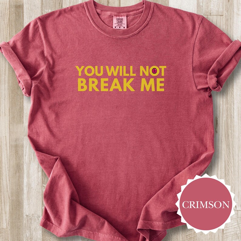 May include: Crimson t-shirt featuring the yellow text "YOU WILL NOT BREAK ME". The shirt has a crew neck and rolled-up sleeves. A circular label with the word "CRIMSON" is visible in the bottom right corner.