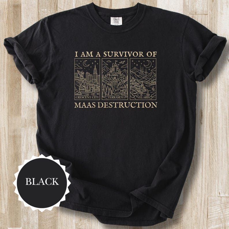 K&ouml;nnte beinhalten: Schwarzes T-Shirt mit goldenem Text und Strichzeichnungen. Der Text lautet &bdquo;I AM A SURVIVOR OF MAAS DESTRUCTION&ldquo; &uuml;ber drei rechteckigen Bildern von Stadtlandschaften und Landschaften. Das Wort &bdquo;BLACK&ldquo; ist auf einem schwarzen Kreis aufgedruckt.