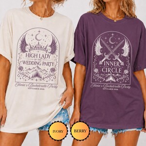 Puede incluir: Dos camisetas de manga corta en colores marfil y baya. La camiseta marfil presenta un gr&aacute;fico morado con una corona, alas y el texto High Lady of the Wedding Party. La camiseta baya muestra espadas cruzadas, alas y el texto Inner Circle.