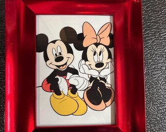 May include: A red picture frame with a glossy finish, featuring a cartoon image of Mickey and Minnie Mouse. The frame has decorative silver embellishments in the corners. The image shows Mickey Mouse in red shorts and yellow shoes, and Minnie Mouse with a bow.