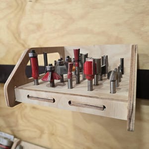 Könnte beinhalten: Ein Holz-Fräser-Organizer mit verschiedenen Fräsern. Die Fräser sind silber und rot und in einem Holzregal angeordnet. Das Regal ist an einer Holzwand befestigt.
