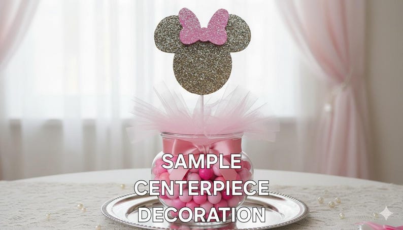 May include: A decorative centerpiece featuring a glass jar filled with pink candies, topped with a glittery mouse head and pink bow. The jar is adorned with a pink ribbon and tulle. Text on the jar reads "SAMPLE CENTERPIECE DECORATION."