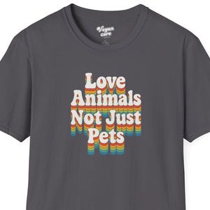 Puede incluir: Camiseta gris oscuro con el texto "Love Animals Not Just Pets" en una fuente retro. El texto está en tonos de rojo, naranja, amarillo y azul. La camiseta tiene cuello redondo y mangas cortas.