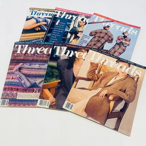 May include: A collection of "Threads" magazines, featuring various covers with images of sewing projects, fashion, and techniques. The magazines display a range of colors and designs, with text such as "Couture Pillows" and "Amish Quilts."