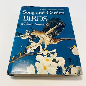 May include: A vintage book titled "Song and Garden BIRDS of North America" by the National Geographic Society. The cover features a bird in flight with a branch of white flowers against a blue background. The book is slightly worn.