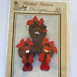 May include: A craft pattern package featuring three handmade cat and bear ornaments. The ornaments are made of felt and have red bows. The package has the text "Hemer House Designs".