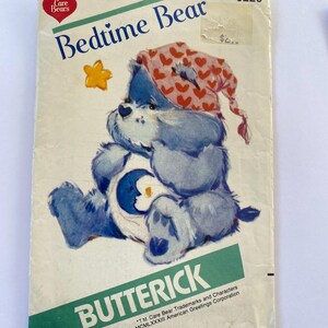 May include: A vintage sewing pattern featuring a blue Care Bear wearing a pink and white nightcap. The pattern is titled "Bedtime Bear" and is from Butterick. The text "*TM Care Bear Trademarks and Characters MCMLXXXIII American Greetings Corporation" is printed at the bottom.