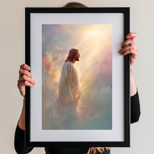 Puede incluir: Una impresión de arte mural enmarcada que muestra el perfil de una figura de pelo largo con una túnica blanca, de pie entre nubes suaves y etéreas. Una luz dorada brillante desciende desde arriba, iluminando la escena con un brillo cálido.