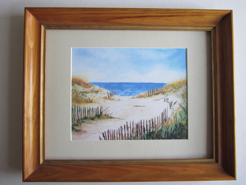May include: A watercolor painting of a beach scene with a wooden fence leading to the ocean. The sky is blue with white clouds and the water is a deep blue. The sand is white and there are some green plants in the foreground.