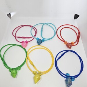 May include: A collection of six colorful necklaces. Each necklace features a cord in a different color: red, blue, green, yellow, pink, and purple. Each necklace has a glittery pendant in a matching color.