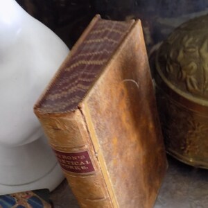 May include: A vintage, brown leather-bound book with gold lettering on the spine that reads "Eaton's Critical Works."