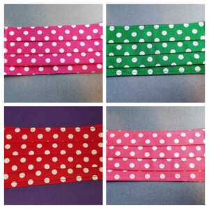 Peut inclure: Quatre masques en tissu avec des pois blancs sur fond rose, vert, rouge et rose. Les masques sont plissés et ont une couture cousue autour des bords.