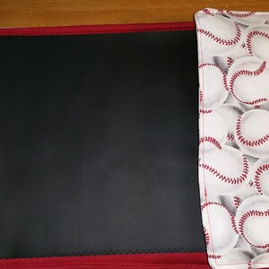 Könnte beinhalten: Ein rot-schwarzes Platzset mit einer schwarzen, gesteppten Oberfläche und einer weißen Stoffklappe mit einem Baseballmuster. Die Klappe hat einen roten, gesteppten Rand.