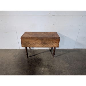 May include: A brown wooden drop leaf table with turned legs. The table is closed and has a rectangular top.