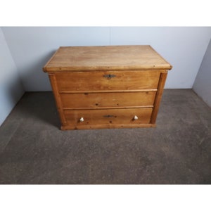 Puede incluir: Un cofre de madera con tres cajones y una tapa con bisagras. El cofre está hecho de madera marrón claro y tiene tiradores de metal simples.